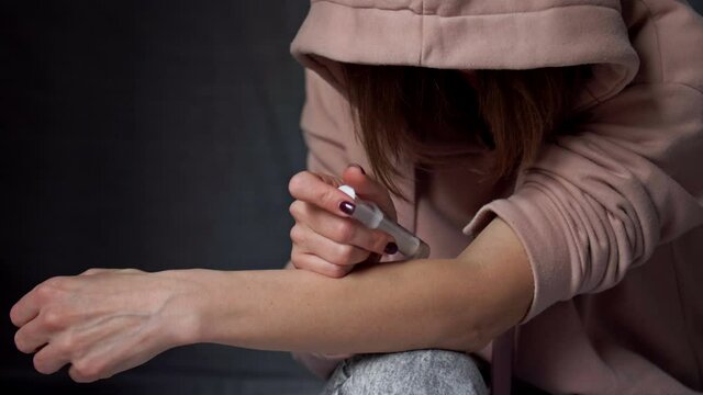 Woman injecting drug into her arm with a syringe.