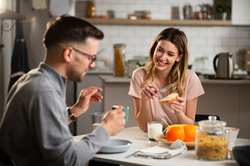 Beautiful young woman enjoying in breakfast with boyfriend. Happy young couple drinking coffee and eating sandwich at home..