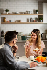 Beautiful young woman enjoying in breakfast with boyfriend. Happy young couple drinking coffee and eating sandwich at home..