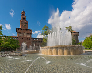 Main entrance to the Sforza Castle - Castello Sforzesco and fountain in front of it, sunny day and clouds in the sky,Milan, Italy
