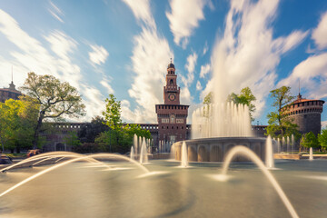 Fototapeta premium Main entrance to the Sforza Castle - Castello Sforzesco and fountain in front of it,long exposure photo, sunny day and clouds in the sky,Milan, Italy