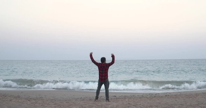 Adventurous man runs along the beach in casual clothes and raises his arms as a sign of joy, freedom. Vacation, adventure, travel