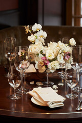 beautifully set table with transparent glasses and a floral arrangement of white orchids and other white flowers in the center