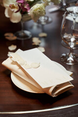 Naklejka na ściany i meble a napkin and a cardboard box with a menu on a plate surrounded by transparent glasses and white petals. selective focus