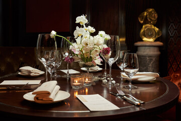 table setting in a dark room of the restaurant. in the center is a composition of white flowers