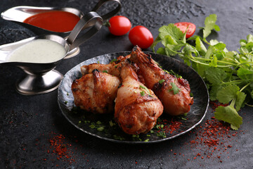 Fried chicken legs with fresh herbs, coriander, vegetables, onions, spices and sauces on a black plate. Background image, copy space