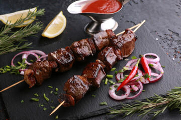 Fried liver shish kebab with lard on skewers with rosemary, lemon, fresh vegetables, herbs and tomato sauce on black table. Background image, copy space