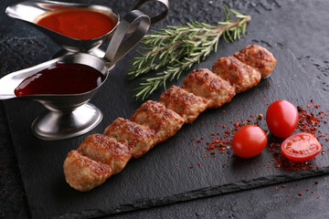 Shish kebab, barbecue. Meat lula-kebab on a black table. Fried minced meat with fresh vegetables, tomatoes, spices and rosemary and sauce. Background image, copy space