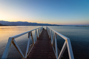 A wooden and metal path into the Red Sea, at the end sits a fisherman with a fishing rod, sunrise