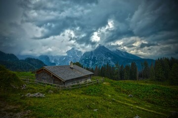 cloudy and stormy day on alpine hut on pasture in front of wood and mountains with clouds