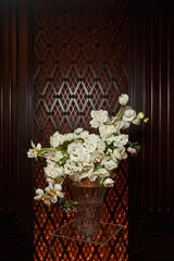 a bouquet of white flowers in a large transparent vase against the background of a dark wooden wall