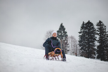 Joyful smile of a young sixteen year old boy riding a historic wooden sled on a ski slope. Dangerous driving. Enjoying the fallen snow in winter. Fooling around at a young age. Immortality