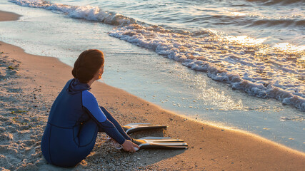 A girl free diver sits on the sea shore puts on her fins and prepares to snorkeling dive. Travel...