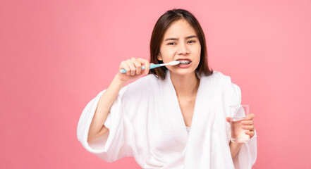 Asian woman wearing braces with brushing teeth and holding water glass, towel on the shoulder on pink background, Concept oral hygiene and health care.