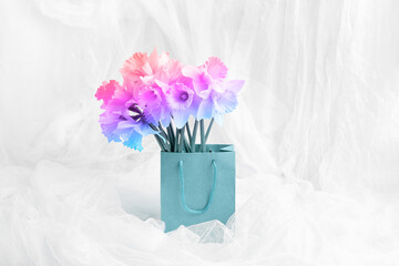 shopping bag with a bouquet of delicate spring flowers on the background of drapery from fabric. holiday gift concept. rainbow gradient toning