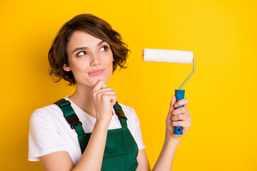 Photo of unsure nice brown hair lady hold roller wear uniform isolated on yellow background