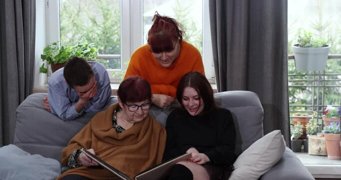 Happy family looking at a photo album. Granny and mother showing photo album pictures to grandchildren , family history