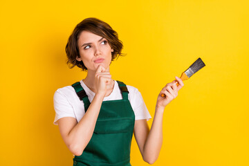 Photo of unsure nice brown hair lady hold brush look empty space wear uniform isolated on yellow...