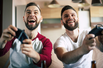 Excited smiling men playing in video games on tv at home on the couch. Friends with joysticks play...