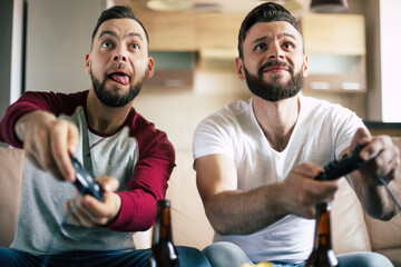 Excited smiling men playing in video games on tv at home on the couch. Friends with joysticks play...