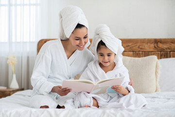 Joyful mother and daughter in bathrobes reading fairy tales