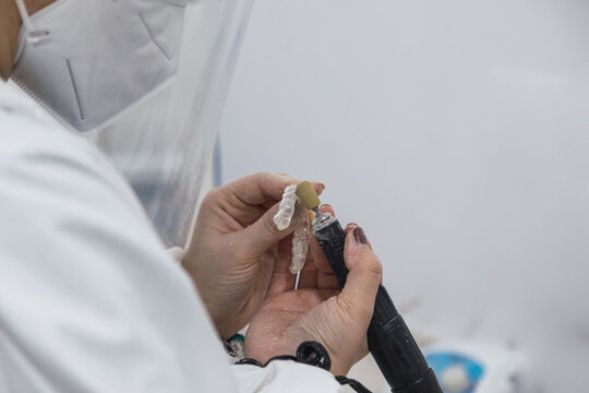 Hands of a dental technician with surgical mask and glasses polishing dentures on his table. health concept.
