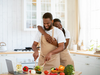 Romantic African American Spouses Wearing Aprons, Cooking Healthy Food Together In Kitchen