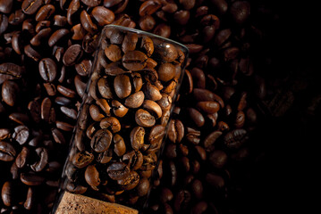 Coffee beans close up. Coffee in a glass jar on a wooden board. Coffee texture on a black shabby table. Contrasting dramatic light as an artistic effect.