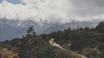 Naklejka premium Hombre practicando senderismo en un camino de la Sierra de Guadarrama en el Parque Nacional de Guadarrama con Cabezas de Hierro de fondo un día nublado de primavera