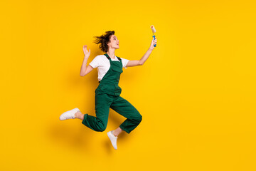 Fototapeta na wymiar Full size photo of happy smiling excited crazy woman painter jumping looking at roller isolated on yellow color background