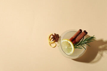 Glass of lemonade with cinnamon and rosemary on beige background