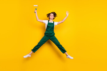 Fototapeta na wymiar Full size photo of happy excited good mood girl painter hold roller jumping in star pose isolated on yellow color background