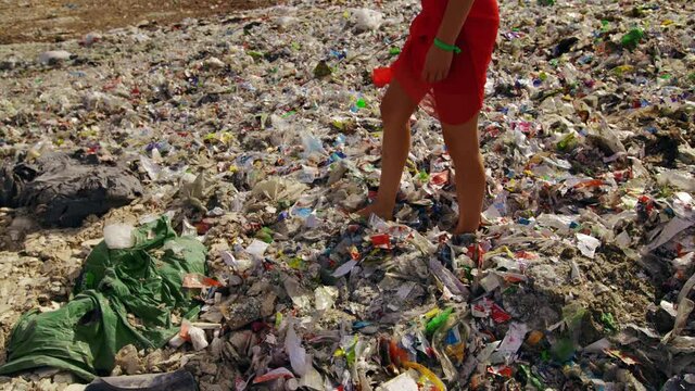 Young barefeet woman carefully walks over huge pile of trash