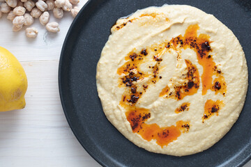 Home made hummus bowl, decorated with boiled chickpeas, lemon and olive oil over a rustic white background.