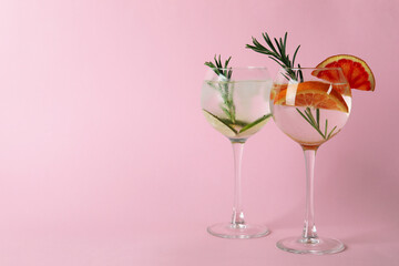 Glasses of cocktails with citrus on pink background