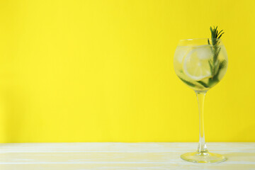 Glass of cocktail with lemon and rosemary on yellow background