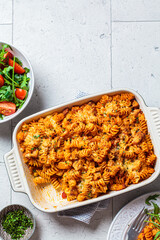 Baked pasta with chicken and cheese in oven dish with green salad, top view, gray background....