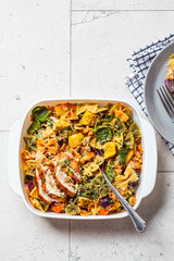 Farfalle pasta with baked vegetables and chicken in white dish, top view, gray background.