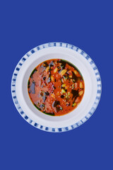 Gazpacho (vegetable soup) in beautiful plate isolated on blue background. Space for text. Photo for menu and site.