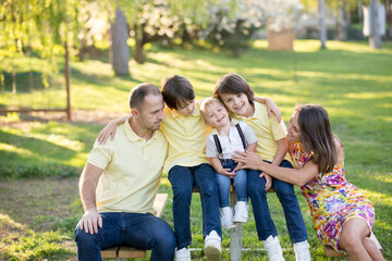 Fototapeta premium Beautiful family, mother, father and three kids, boys, having familly outdoors portrait taken on a sunny spring evening, beautiful blooming garden, sunset time