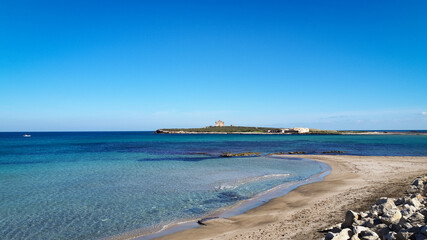 Small beach in Portopalo town, Sicily with the Capo Passero island and its fortress in background