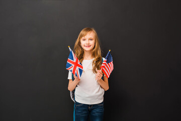 Happy blond child girl 8-9 y.o. holds a miniature of the English and American flag. Learn English...