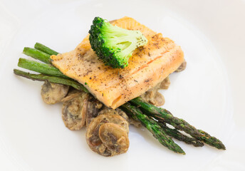 dish of fried river trout fillet with garnish of broccoli, asparagus sprouts and mushroom sauce on white background