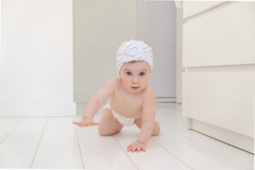 Cute little funny caucasian blonde baby girl wearing a white turban hat , crawling on fours on...