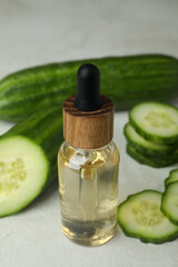 Bottle of cosmetic oil and cucumbers on white textured background
