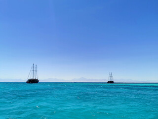 Obraz premium Two masted ships near coral reefs in the Red Sea. Tourist walks by the sea on a sunny day
