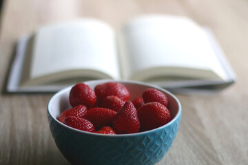 Bowl of fresh strawberries and open book on a table. Selective focus.