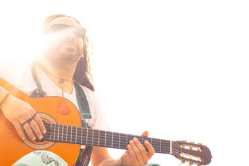 Hippy man with beard and glasses playing guitar outdoors on the beach