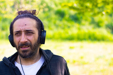 Hippy man with beard and headphones listening music outdoors on the garden