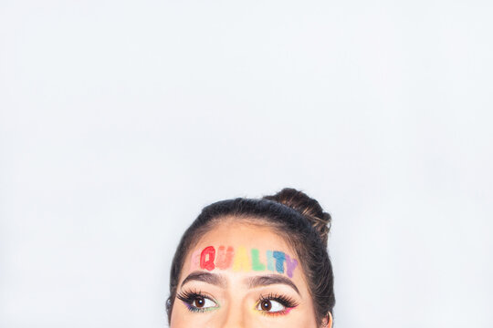 Phrase 'equality' written on the forehead of a beautiful girl in gay pride makeup, with copy space.